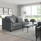 Modernes Wohnzimmer mit grauem VINLIDEN-Sofa, Kissen und Couchtisch mit Blumen.