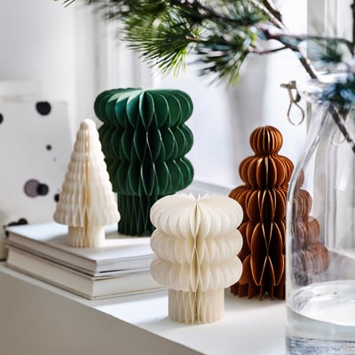 Vier bunte Papierwaben-Weihnachtsbäume in Grün, Weiß und Braun stehen auf einem Regal, wobei einer kleiner ist und so eine festliche Weihnachtsdekoration bildet.
