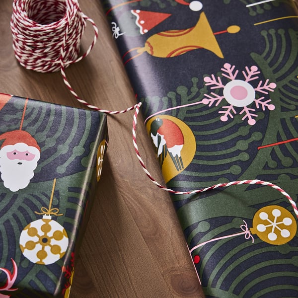 Geschenkverpackung mit festlichen Motiven, darunter Weihnachtsmann, Schneeflocken und Ornamente, die auf einem Holztisch liegen.