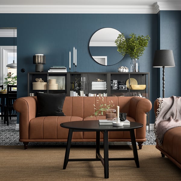Modernes Wohnzimmer mit braunem Ledersofa, dunklem Couchtisch, blauer Akzentwand, schwarzer Stehlampe und dekorierten Bücherregalen.