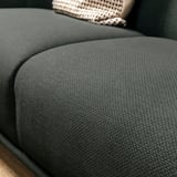 Dunkelgrünes, abgerundetes Stoffsofa, Nahaufnahme, die seinen weichen, strukturierten, einladenden Sitz zeigt.