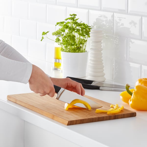 Person schneidet gelbe Paprika auf Holzschneidebrett mit Küchenmesser. Messerset für verschiedene Küchenaufgaben.