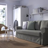 Graues Schlafsofa in der Nähe des Bücherregals, helles Zimmer