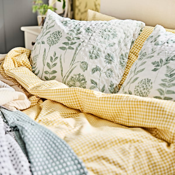 Gemütliches Bett mit einem WEYMOUTH-hohen gelbkarierten Seersucker-Bettdeckenset. Große Bettdecke, grün-blumiges Kissen, bequeme Baumwollmischung.