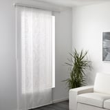 Durchsichtige Vorhänge, die ein Fenster abdecken, lassen Licht herein und bieten gleichzeitig Privatsphäre, mit einer modernen Pflanze und einem Stuhl in der Nähe.