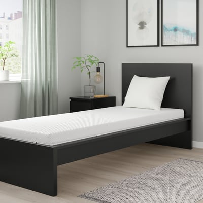 Minimalist bedroom ÅBYGDA black platform bed with white mattress, single size. Accented with modern decor, including grey rug, lamp, and wall art.