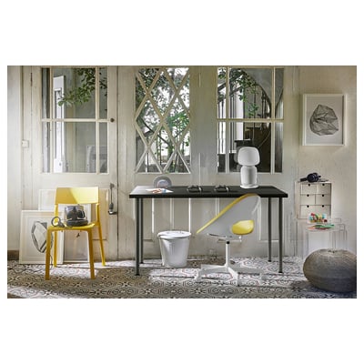 Modern office space with ADILS black desk, yellow chair, and patterned rug, featuring windows and decorations.