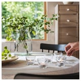 Hand lighting small glass candles on table with flowers and wooden furniture.