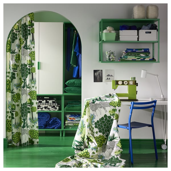 Green-themed craft room with fabric, sewing machine, chair, and shelves filled with supplies.