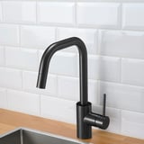 Black kitchen faucet with pull-out spout, set against white brick backsplash, wooden counter, and metal sink.