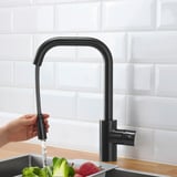 Hand holding black faucet spraying water into sink with fruits and vegetables.
