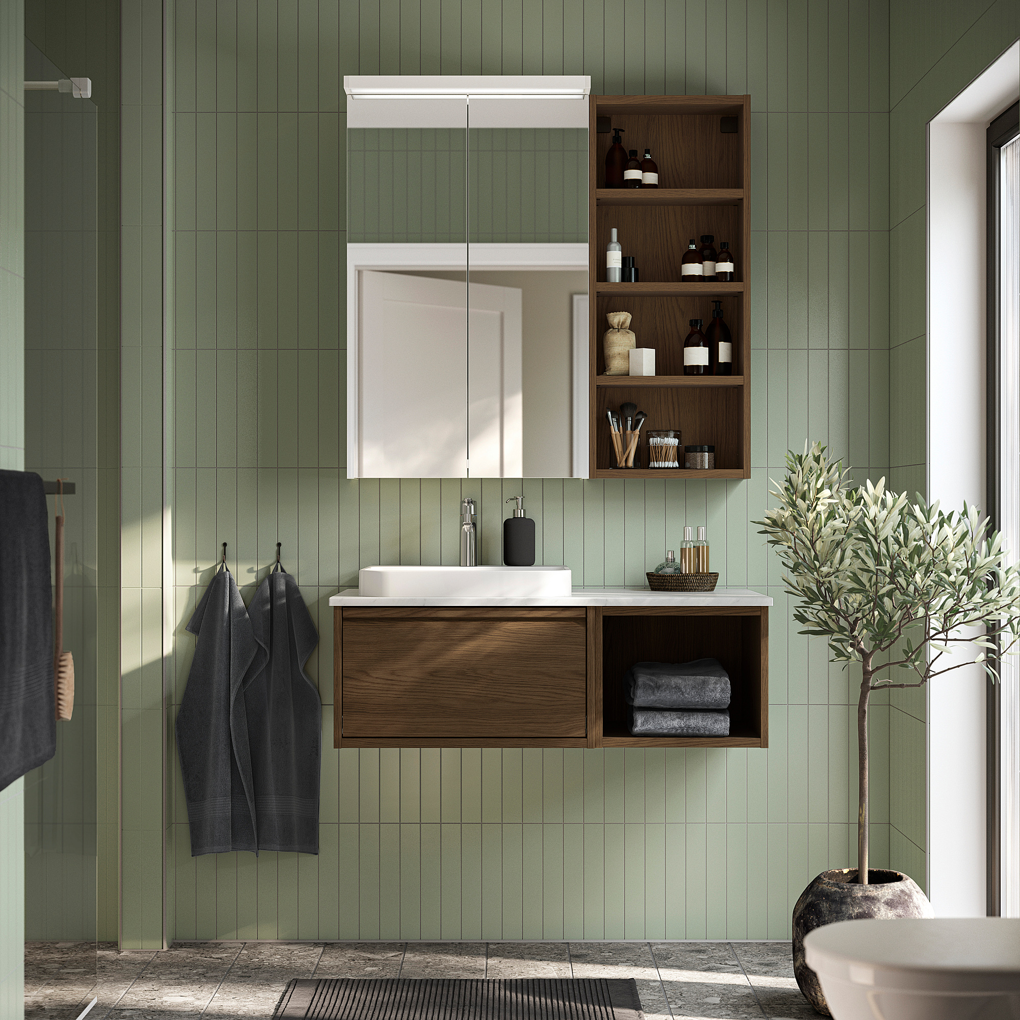 Modern bathroom with brown oak ÄNGSJÖN vanity, marble basin, and open storage. Mirror cabinet and olive tree enhance the stylish, organized look.