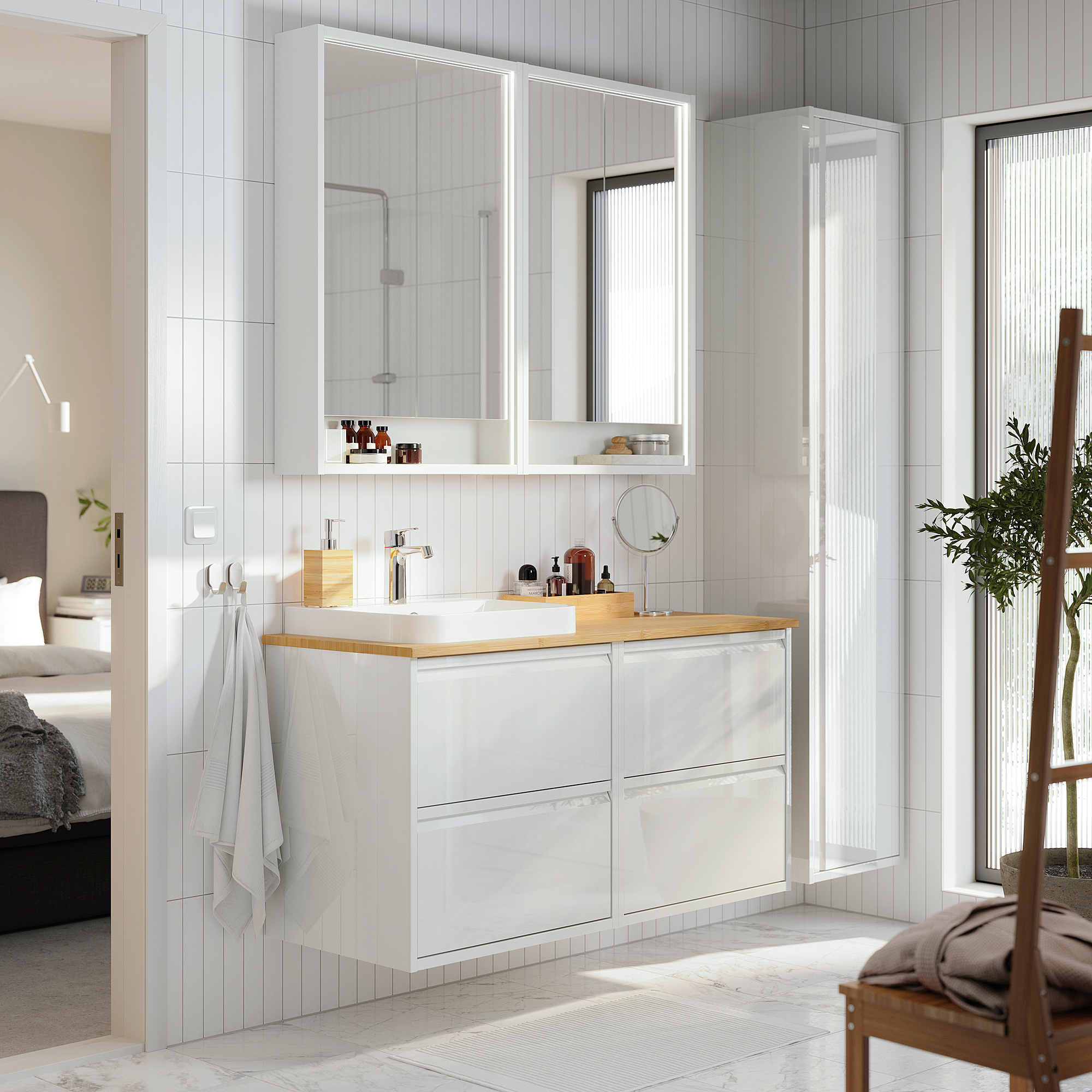 ÄNGSJÖN white bathroom vanity with wood countertop, two mirrors, sink, storage, towel, chair, plant.
