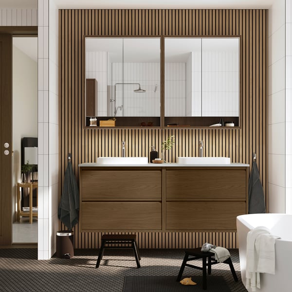 Modern bathroom: brown cabinet, 2 sinks, mirrors, black stool, towels. Minimalist design.