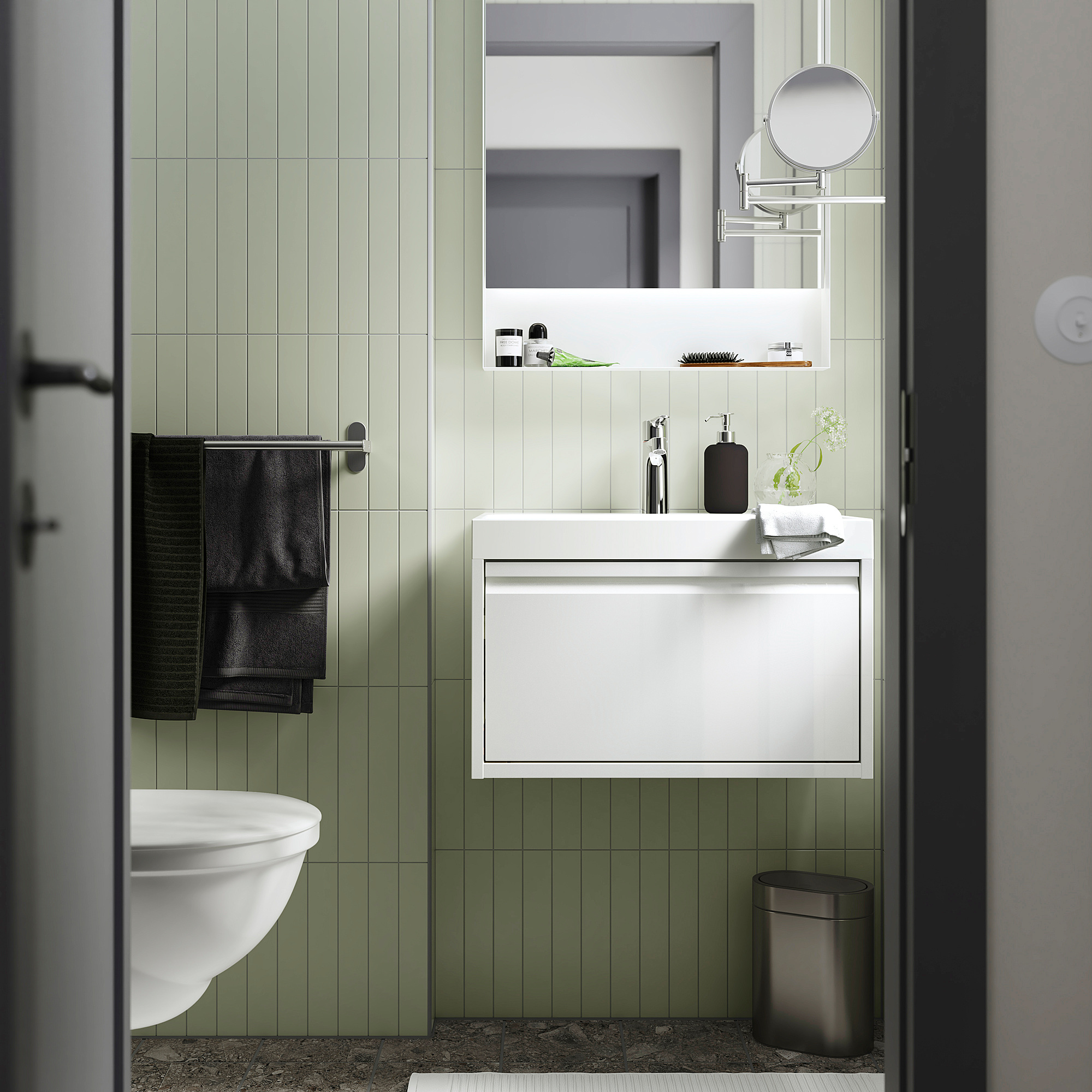 Modern bathroom with white ÄNGSJÖN vanity. Sleek white drawer, appear larger than adjacent toilet. Black towels hang on left.