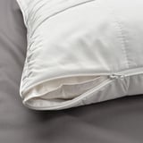 Close-up of a white pillowcase with a zipper partially open. The texture is smooth with a subtle pattern. It lies on a dark, textured bedsheet.