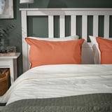ÄNGSLILJA rust orange pillowcase, soft cotton, fits standard pillow, on cozy bed, with white sheets, basket, and nightstand.