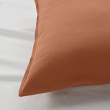 Close-up of soft, textured, rust-colored pillowcase on a bed, showcasing its smooth fabric and envelope closure.