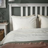 ÄNGSLILJA pillowcases, light beige, soft cotton, rectangular, on bed, with headboard. Neutrally styled, cozy bedroom.