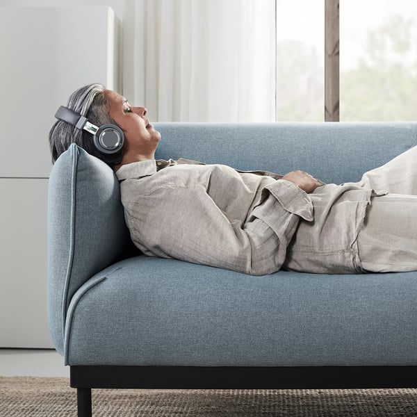 Person relaxing on blue ÄPPLARYD sofa with headphones.
