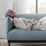 Person relaxing on blue ÄPPLARYD sofa with headphones.
