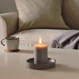 A lit candle in a dish on a coffee table, next to a mug and spoon, with a cozy couch in the background.