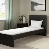 Modern minimalist bedroom with black bed, white pillow, cream rug, beige walls, and green curtains.