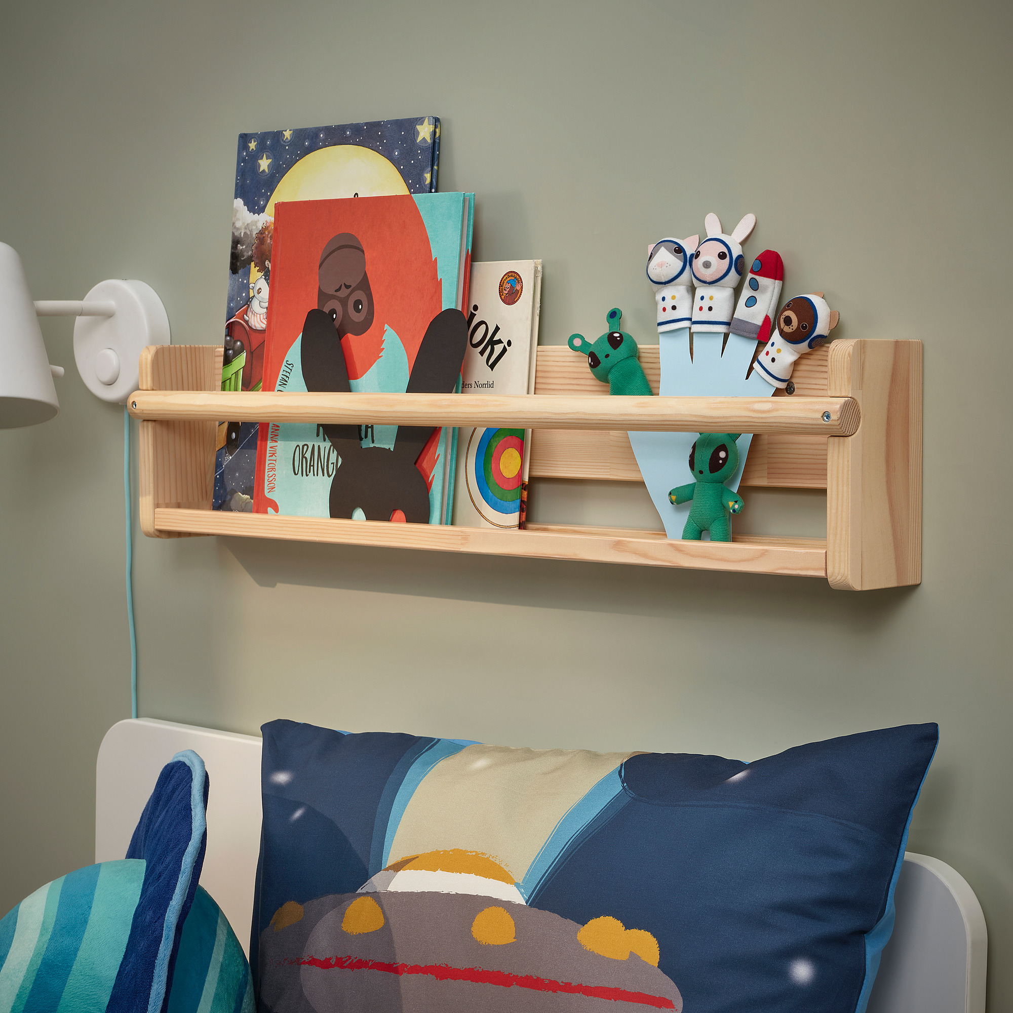 Wooden shelf AFTONSPARV holds colorful books and playful figurines above a bed with blue pillows.