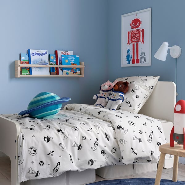 Cozy kids space-themed bedroom with astronaut bedding, plush toys, books, and robot art.