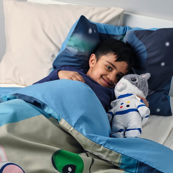 Boy in bed with plush gray cat in blue suit, galaxy sheets.