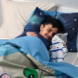 Boy in bed with plush gray cat in blue suit, galaxy sheets.
