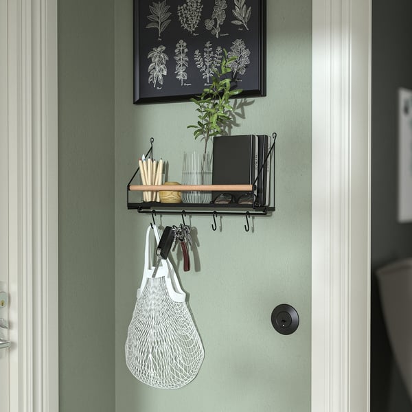 A narrow wall organizer in green with hooks and a shelf. It holds keys, a white bag, and other small items.