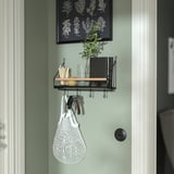 A narrow wall organizer in green with hooks and a shelf. It holds keys, a white bag, and other small items.