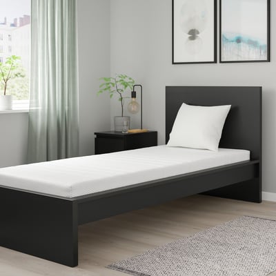 Modern bedroom with black bed, white pillow, grey curtains, black nightstand, and wall art.