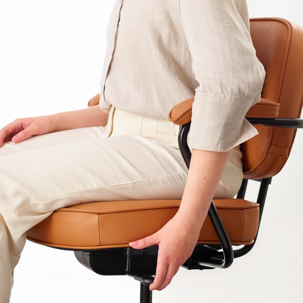 Person sitting in an ergonomic office chair with adjustable lumbar support and padded armrests, featuring leather upholstery.
