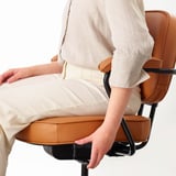 Person sitting in an ergonomic office chair with adjustable lumbar support and padded armrests, featuring leather upholstery.