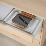 Wooden desk drawer with notebook, pen, and paper, indicating storage and organization.