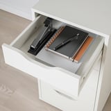 Open white desk drawer with black stapler, notebook, and pen. Finished back and sides.