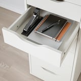 Open white ALEX drawer revealing a notebook, pen, and stapler, organized for desk use.