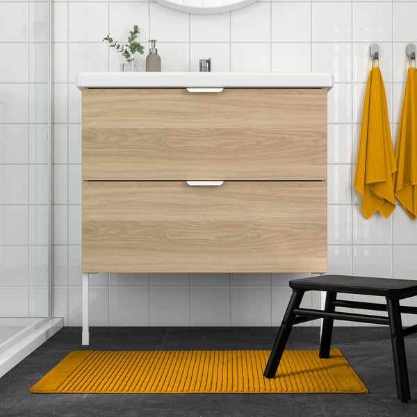 Golden yellow cotton bath mat in modern bathroom, soft & absorbent, complements yellow towels & wooden vanity.