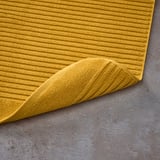 Mustard yellow bath mat made of pure cotton terry. Its structured weave massages feet, absorbs well, and dries quickly.