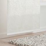 White sheer curtain with leaf pattern on wall, covering window. Soft, speckled rug on wooden floor.