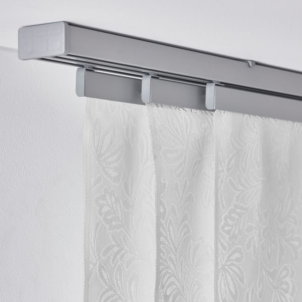 Silver curtain rail with leaf-patterned white panels, filtering sunlight, mounted on wall.