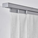 Silver curtain rail with leaf-patterned white panels, filtering sunlight, mounted on wall.