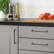 Modern kitchen with nickel-plated ANDERSFORS handles on gray drawers. Dark countertop with tomatoes, herbs, and stylish oil dispensers.