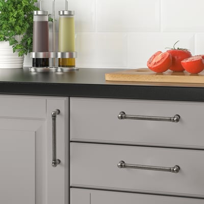 Modern kitchen with nickel-plated ANDERSFORS handles on gray drawers. Dark countertop with tomatoes, herbs, and stylish oil dispensers.
