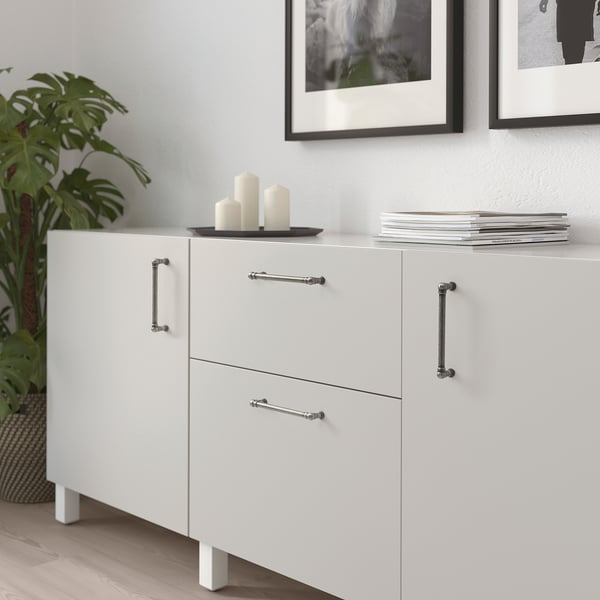 White cabinet with silver ANDERSFORS handles, sleek and minimalist design. Its larger than the potted plant and smaller than the stacked books.