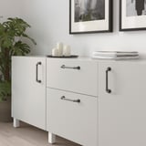 Modern, white cabinet with ANDERSFORS silver handles, black and white decor, plant on left, small on white floor.
