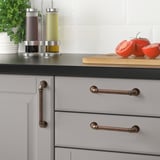 Modern kitchen with ANDERSFORS bronze handles on gray cabinets. Stainless dispensers, tomatoes, and parsley on counter.