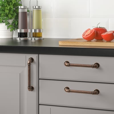 Modern kitchen with ANDERSFORS bronze handles on gray cabinets. Stainless dispensers, tomatoes, and parsley on counter.